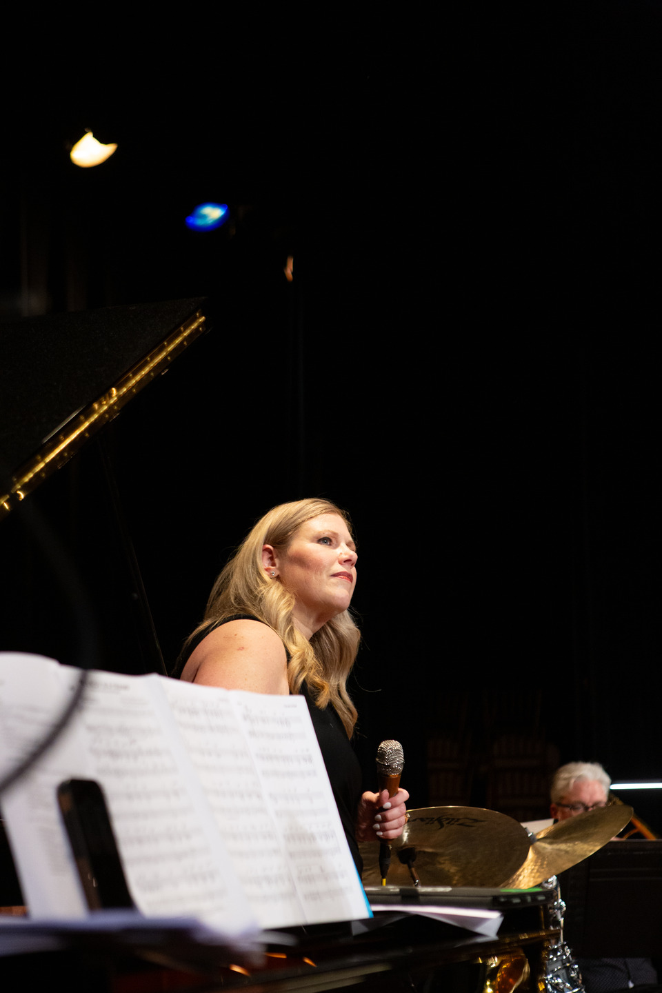 A low-angle portrait of the vocalist mid-song, lit against the dark stage beside the grand piano.